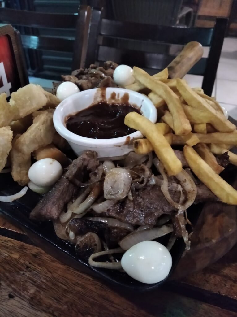 Porción mixta de papas, mandioca, carnes, huevos de codorniz y al centro salsa barbecue.